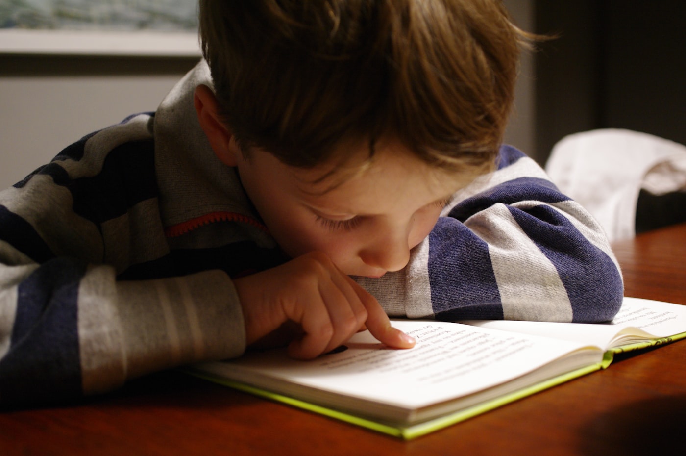 A boy leaning on a table reading an open book