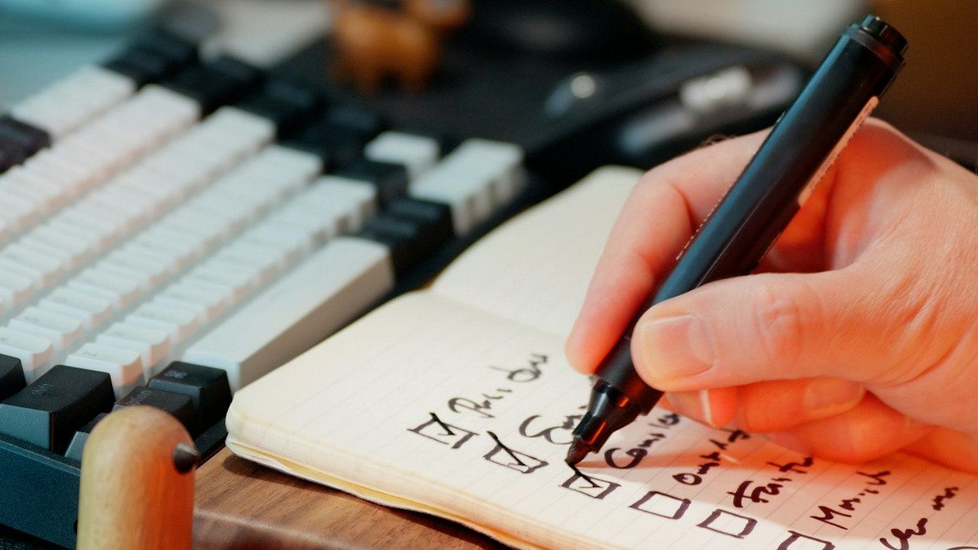 A hand writing a checklist in a notebook at a desk